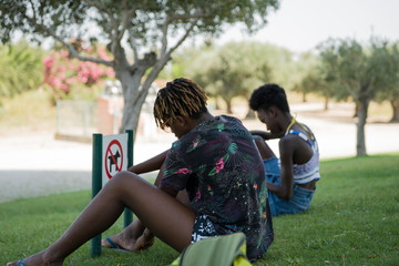 Two African girls sitting on the grass in the vicinity of Lisbon. In the background is a blurred image of trees. Selective focus.