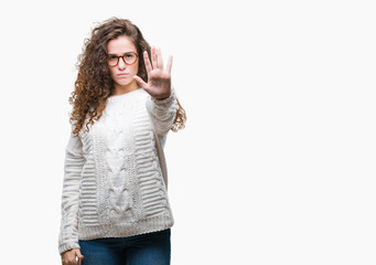 Poster - Beautiful brunette curly hair young girl wearing winter sweater over isolated background doing stop sing with palm of the hand. Warning expression with negative and serious gesture on the face.