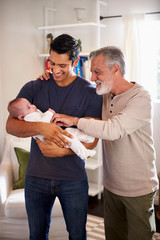 Wall Mural - Proud senior Hispanic man standing with his adult son holding his four month old boy, vertical