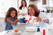 © Monkey Business - Young girl making a cake in the kitchen with her grandmother, mum stands watching, selective focus