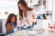 © Monkey Business - Young Hispanic girl making cake in the kitchen with help from her mum, waist up