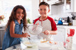 © Monkey Business - Brother and sister preparing cake mixture together at the kitchen table looking to camera, waist up