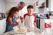 © Monkey Business - Brother and sister standing at the kitchen table mixing cake mix with their grandfather, close up