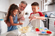 © Monkey Business - Brother and sister standing at the kitchen table making cake mix with their grandfather, close up