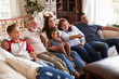 © Monkey Business - Three generation Hispanic family sitting on the sofa watching TV, grandmother using remote control