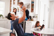 © Monkey Business - Young Hispanic family in their kitchen, dad lifting baby in the air, mum cooking at hob, close up