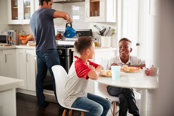 Wall Mural - Two pre-teen male friends sit talking in kitchen at one boyÕs house, dad in the background