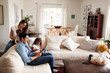 © Monkey Business - Young Hispanic family sitting on sofa reading a book together in their living room