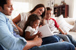 © Monkey Business - Young Hispanic family of four sitting on the sofa reading book together in their living room