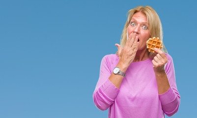 Wall Mural - Middle age blonde woman eating sweet waffle over isolated background cover mouth with hand shocked with shame for mistake, expression of fear, scared in silence, secret concept