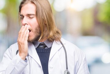 Sticker - Young handsome doctor man with long hair over isolated background bored yawning tired covering mouth with hand. Restless and sleepiness.