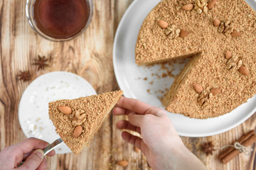 Homemade sweet layered honey cake with nuts on white plate on wooden table with bowl of honey, cinammon and badian.