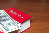 Fototapeta Paryż - a lot of dollars on a red book. on the book the inscription business. The concept of business success, business acumen, success, wealth. copy space.