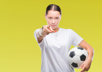 Young beautiful caucasian woman holding soccer football ball over isolated background pointing with finger to the camera and to you, hand sign, positive and confident gesture from the front