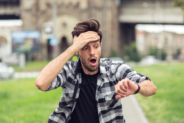 young man running late for his meeting, looks at the time on his watch, feeling stressed and sprinti