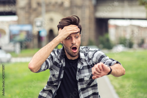 Fotomural Young man running late for his meeting, looks at the time on his watch, feeling