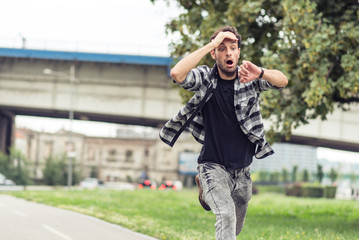 Young man running late for his meeting, looks at the time on his watch, feeling stressed and sprinting to his meeting