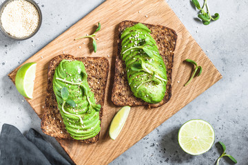 Top view on two toasts with avocado on a wooden tray on a table. The concept of vegetarian and healthy diet food.