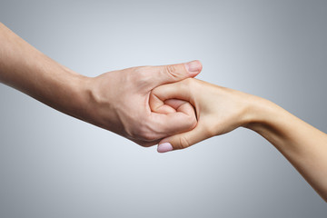 Male and female hands united in a handshake on gray background