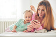 © sata_production - Young mother and her baby daughter using smart phone in bed