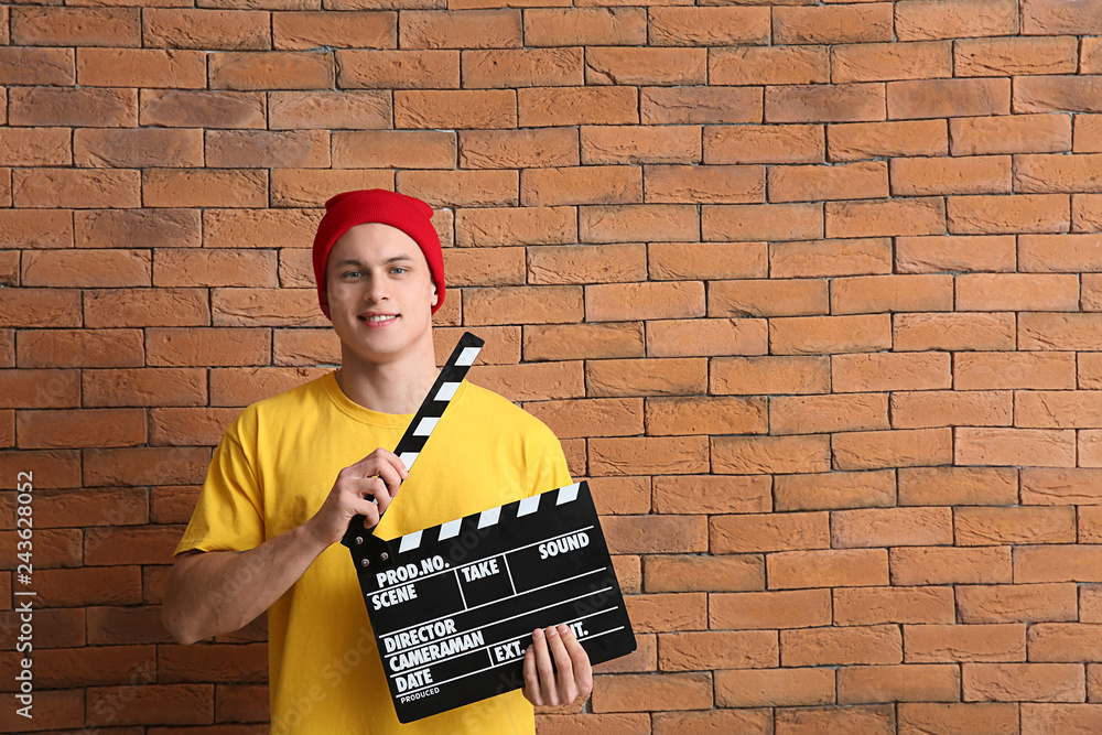 Young man with clapperboard against brick wall