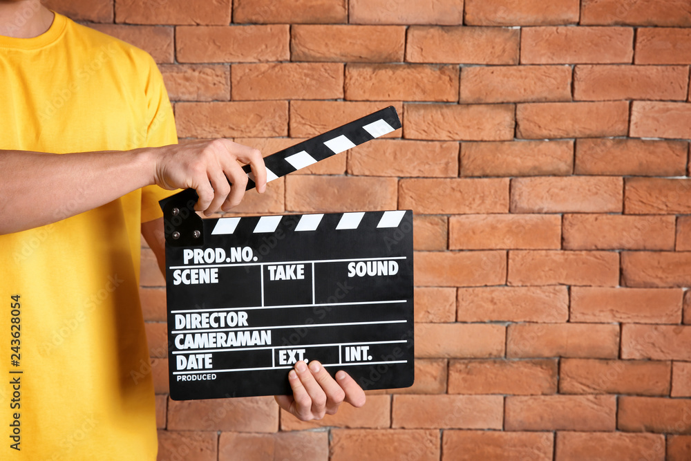 Young man with clapperboard against brick wall