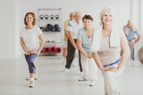 Fototapeta  - Smiling senior woman exercising with group of active seniors in fitness center