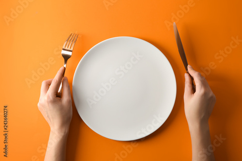 Fotografia  Female hands with cutlery and empty plate on color background