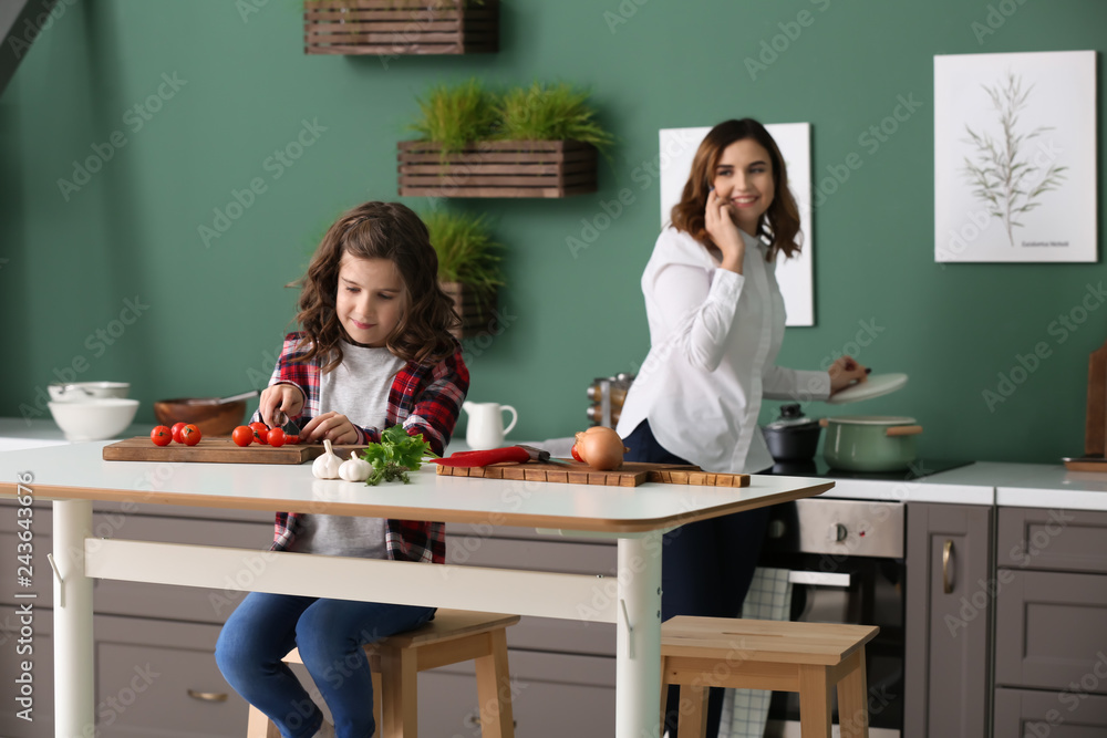 Busy mother cooking with daughter while working at home