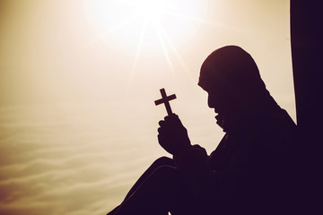 Canvas Print - concept of religion. Silhouette of a man praying with a cross in hand at sunrise.