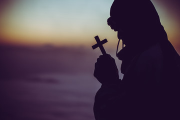 Canvas Print - concept of religion. Silhouette of a man praying with a cross in hand at sunrise.