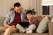 © Syda Productions - family, fatherhood, technology and people concept - happy father and little son with tablet pc computer sitting on sofa at home