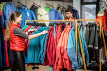 Young Woman Choosing Winter Clothes Picking Up Down Jackets On The Hanger In The Sports Shop