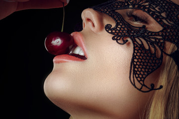 Detail of young woman mouth with cherries against black background.