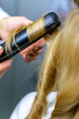 Wall Mural - Close-up photo professional hairdresser uses flat iron for making curls on beautiful blonde hair