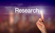 A hand selecting a Research business concept on a clear screen with a colorful blurred background.