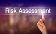 A hand selecting a Risk Assessment business concept on a clear screen with a colorful blurred background.