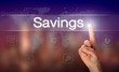 A hand selecting a Savings business concept on a clear screen with a colorful blurred background.