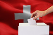 © twinsterphoto - Close-up of human hand casting and inserting a vote and choosing and making a decision what he wants in polling box with Switzerland flag blended in background.