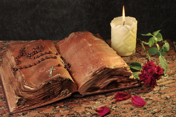 Old bible, crucifix, burning candle on a granite table