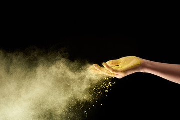 cropped view of adult woman with yellow holi powder on black background