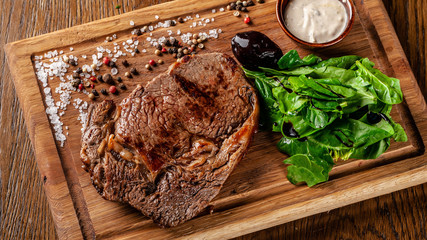 Italian cuisine. Juicy beef meat, veal steak on a wooden board with spinach, prunes and French mustard sauce. On the table is a glass of red pomegranate wine. Serving dishes in the restaurant