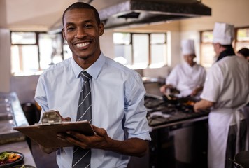 Male manager writing on a clipboard in kitchen