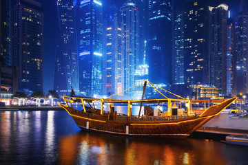 Wall Mural - Beautiful view to Dubai Marina, UAE. Illuminated traditional boat at pier. Long exposure time lapse effect at night