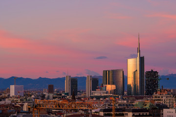 Milan skyline at sunset with modern skyscrapers in Porta Nuova business district in Italy. Panoramic view of Milano city. The mountain range of the Lombardy Alps in the background.