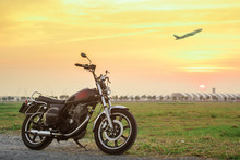 Vintage Motorcycle With Blurry Plane At Sunset.