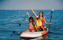 Mother With Two Daughters Stand Up On A Paddle Board