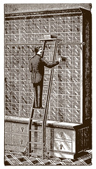 Inside a historical store a salesman standing on a floor track bike ladder and pulling out a box from a huge shelf (after an etching or engraving from the 19th century)