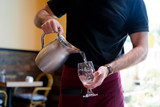Fototapeta Łazienka - The waiter in the restaurant pours the water from the jug into the glass
