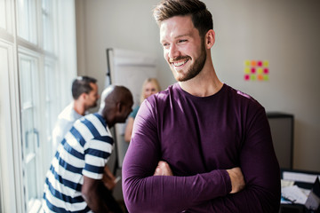 Wall Mural - Young designer smiling with coworkers talking in the background